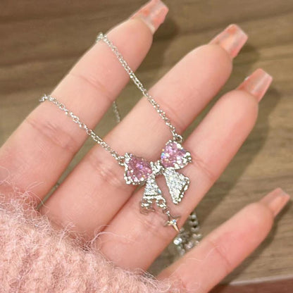 Bow pendant necklace shown in hand: pink bow pendant with dangling star and chain
