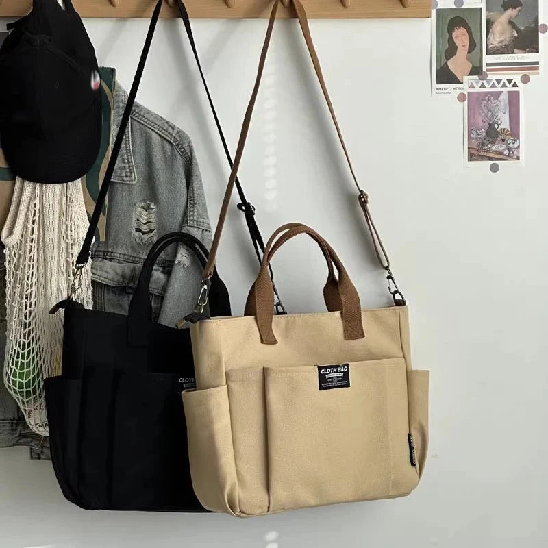 Khaki and black canvas tote bags hanging on hooks, each with crossbody strap and zip pocket