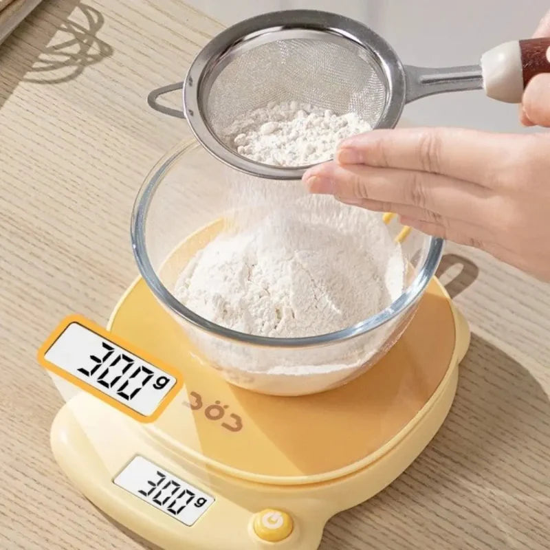 Yellow digital kitchen scale under a sieve above a bowl of flour