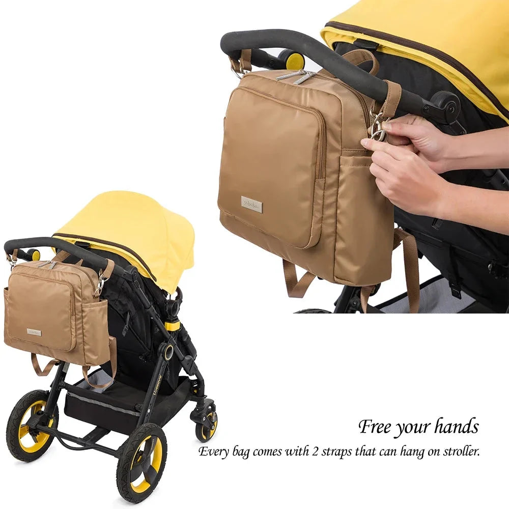Tan diaper bag backpack clipped to a stroller with hanging strap