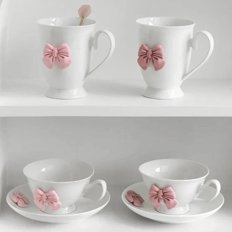 Set of two white tea cups with pink bow ornaments on saucers