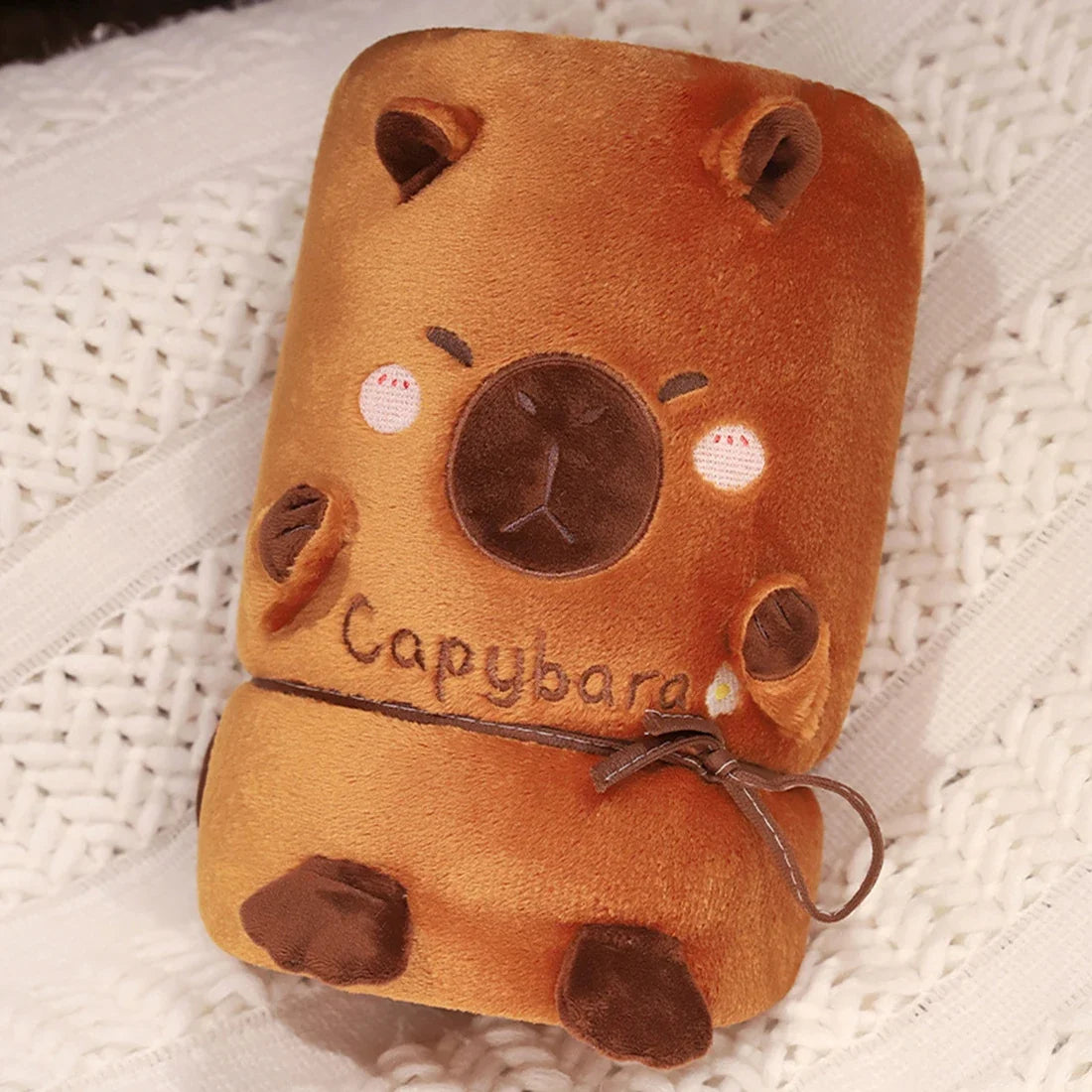 Rolled orange capybara blanket pillow with stitched face, ears, paws, and tie cord.