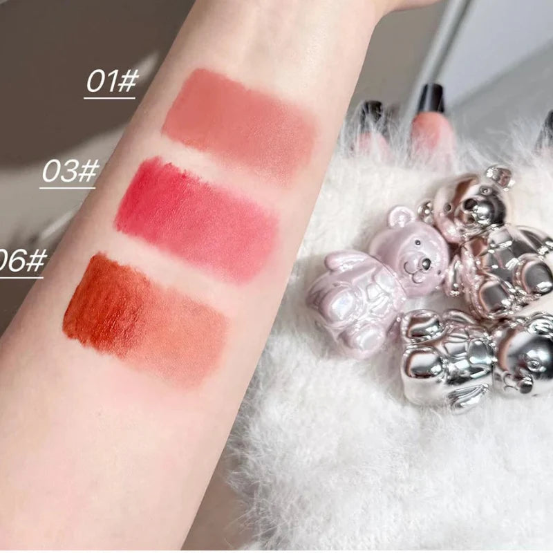 Swatches of lip or cheek shades in peach, red, and orange on skin with compact