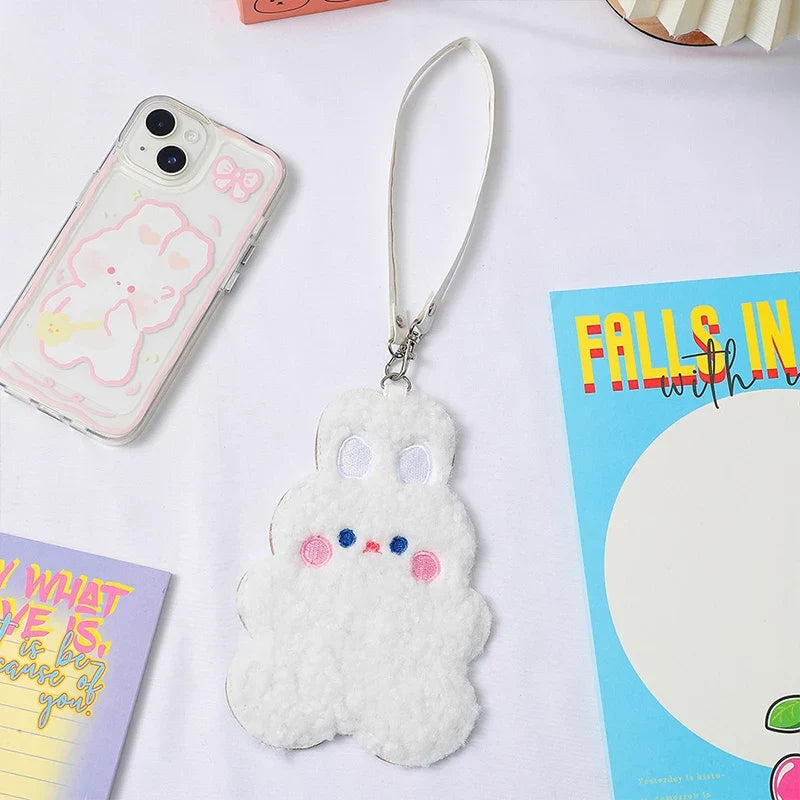 White plush animal photo card sleeve with lanyard strap next to smartphone