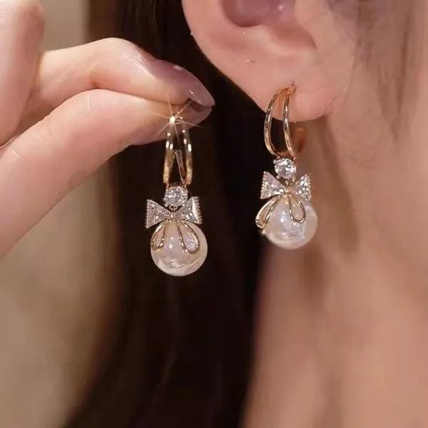 Gold bow and teardrop pearl earrings with rhinestone sparkle