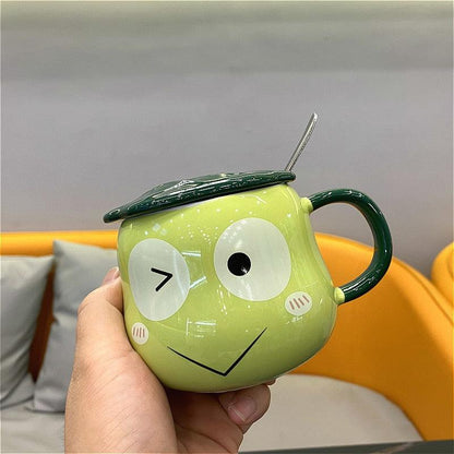 Lime green frog-shaped mug with lid and spoon, hand-held side view with mouth and cheeks
