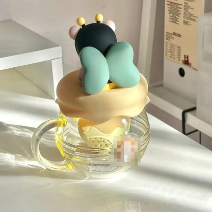 Glass tea infuser mug with bear character topper, mint arms, and honey-yellow lid