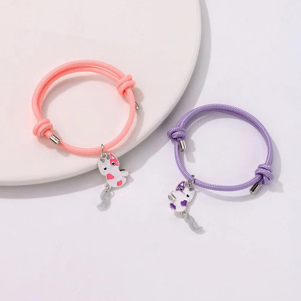 Set of two braided cat bracelets on plate: pink and lavender bands with dangling charm tassels