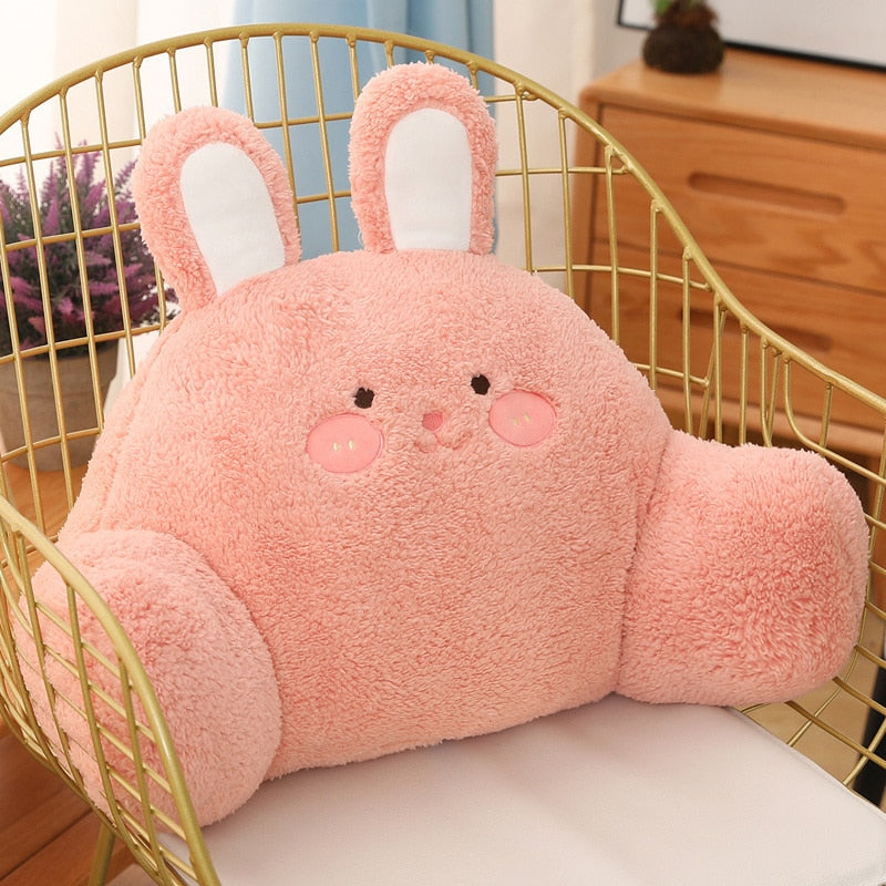 Plush pink bunny cushion with embroidered face and long upright ears in a chair.