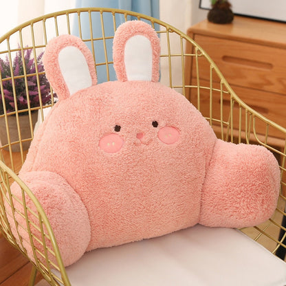 Plush pink bunny cushion with embroidered face and long upright ears in a chair.