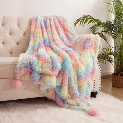 Pastel rainbow fluffy blanket with corner pom-poms laid over a beige sofa backrest