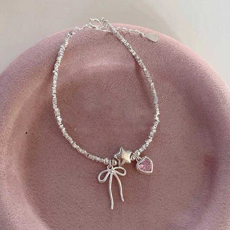 Silver charm bracelet with star, pink heart and bow accents with dangling ribbon