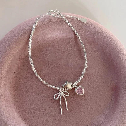 Silver charm bracelet with star, pink heart and bow accents with dangling ribbon
