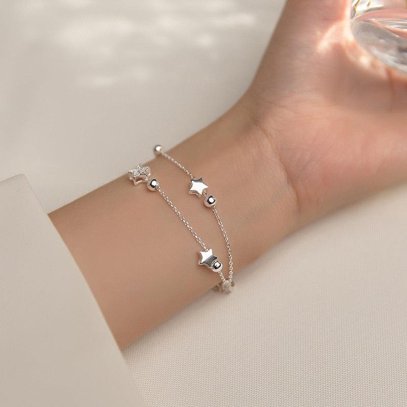 Silver star charm bracelet worn on wrist with dangling star and round bead accents.