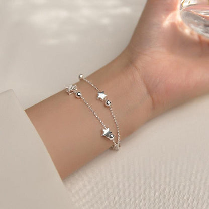 Silver star charm bracelet worn on wrist with dangling star and round bead accents.
