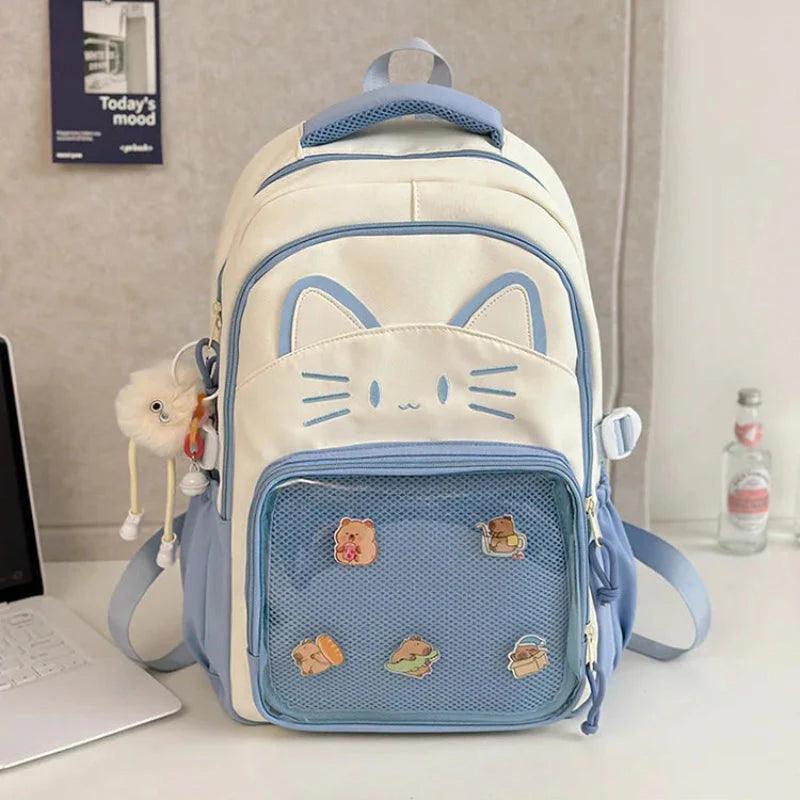 White cat school backpack with blue trim; front mesh pocket with colorful animal patches.