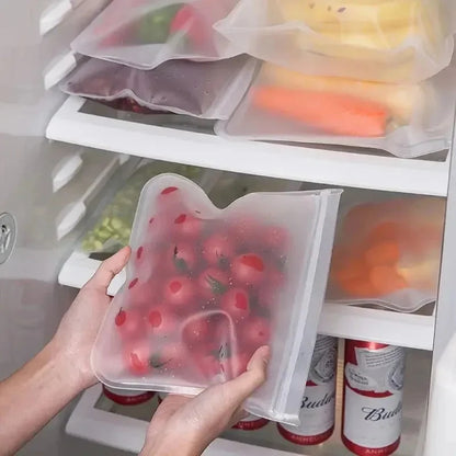 Clear zip-top silicone storage bag with mixed produce, held in a refrigerator