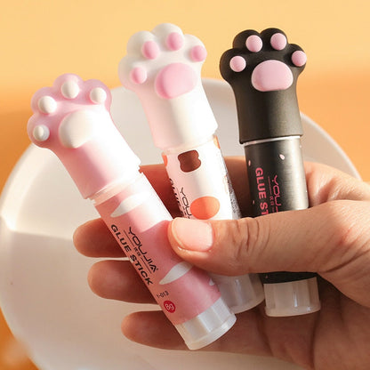 Cat paw glue stick close-up held in hand, pink and white tubes with paw caps