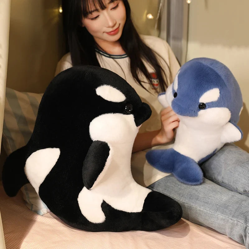 Blue and black dolphin plushies, one held on a couch, soft plush texture