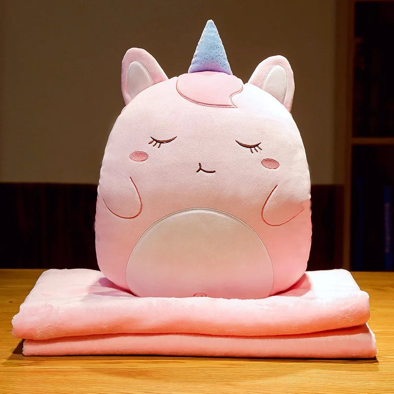 Unicorn animal cushion blanket with light-pink plush face on folded pastel pink blanket layers