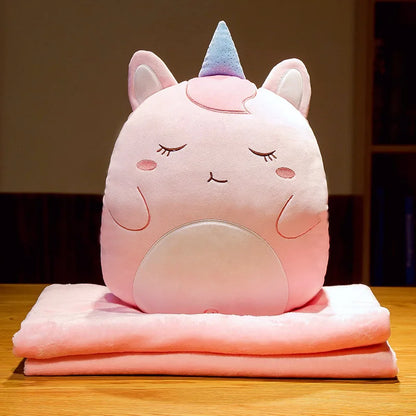 Unicorn animal cushion blanket with light-pink plush face on folded pastel pink blanket layers