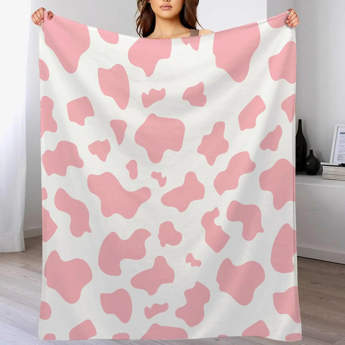 Cow print flannel blanket in pink and white, held up for display
