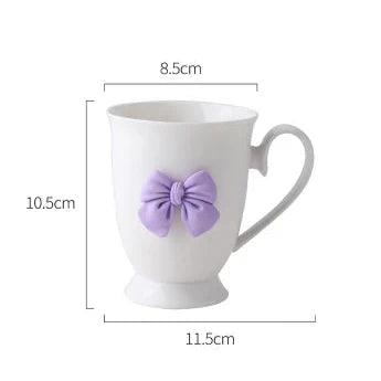 White coffee mug with purple bow on front and curved handle