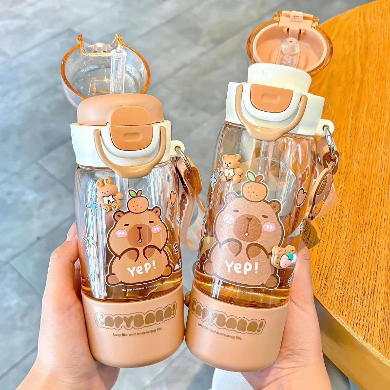 Capybara-themed water bottles in hands, clear body, white cap with orange latch, cute bear face