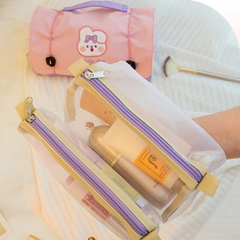 Pink roll-up makeup bag with bear patch beside two long clear zip pouches