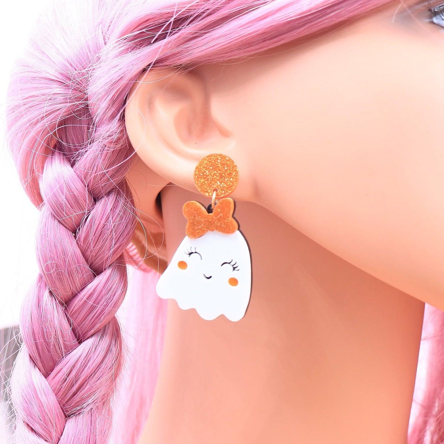 Ghost face earrings worn with pink hair; white ghost shapes with orange glitter crown and bow