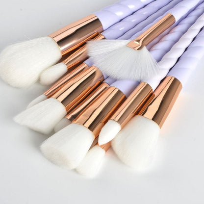 Makeup brushes close-up: white bristles with rose-gold caps and light lavender spiral handles