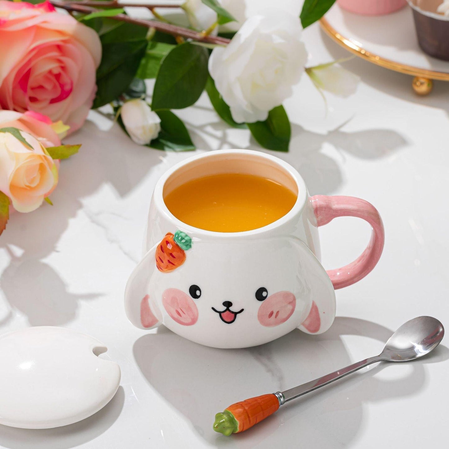 Rabbit ceramic mug with pink handle, orange tea inside, carrot spoon resting beside it.