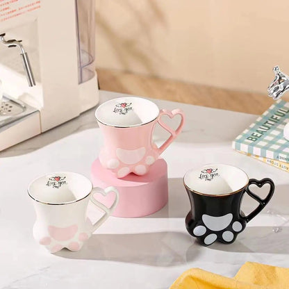 Three cat paw mugs in pink, white, and black with heart handles and paw pad designs