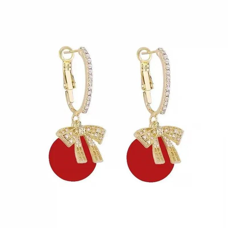 Gold-tone hoop earrings with red ornament ball and bow charm