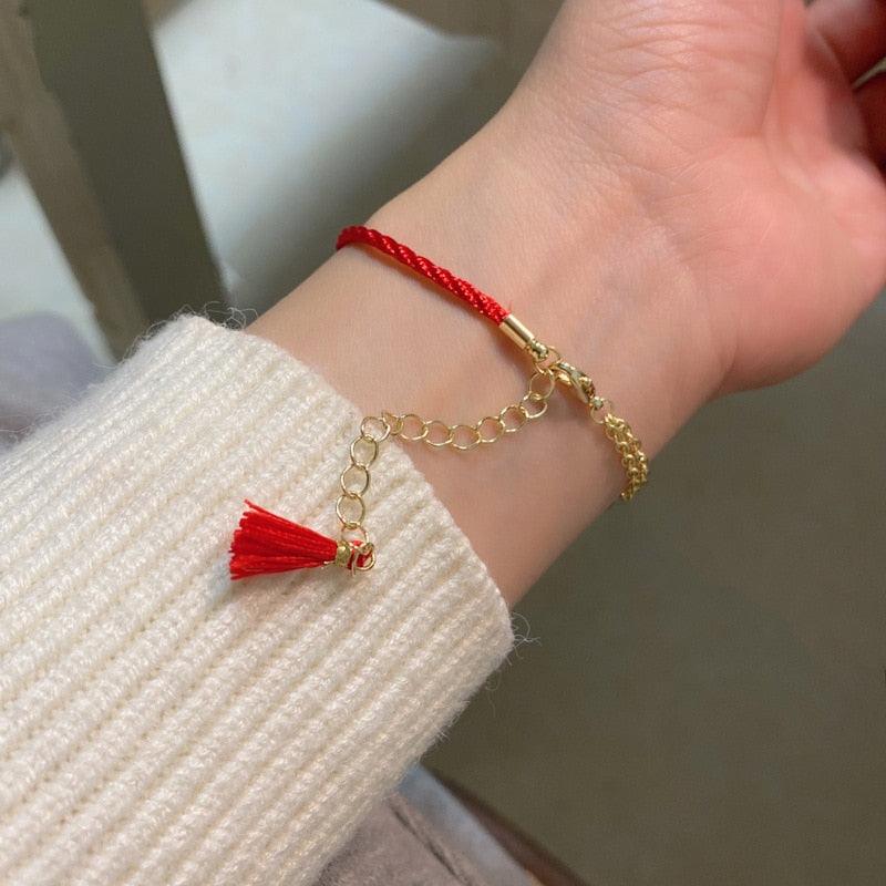 Red cord bracelet with gold chain and fox tassel charm on a wrist