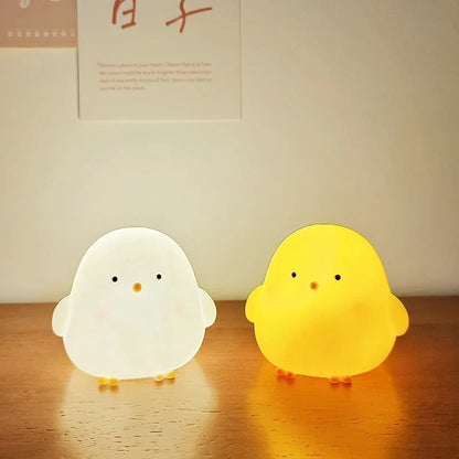Two silicone chick LED night lights, white and yellow, on a wooden tabletop
