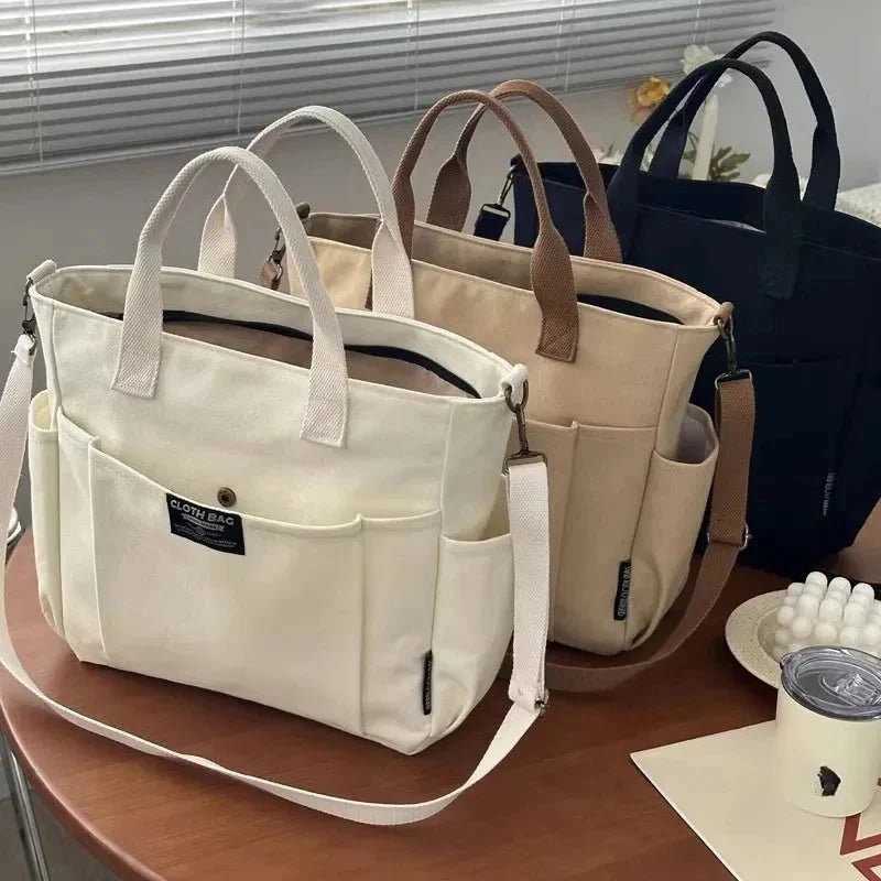 White canvas tote bag with two short handles and long crossbody strap, side zip pockets