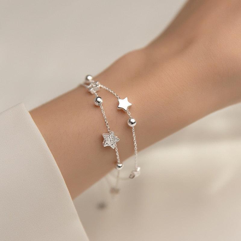 Silver star charm bracelet on wrist featuring a larger star pendant and round bead accents.