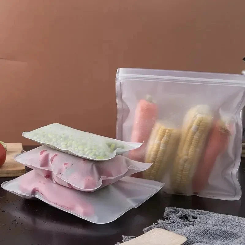 Reusable silicone storage bags with clear zip tops, filled with banana slices and greens