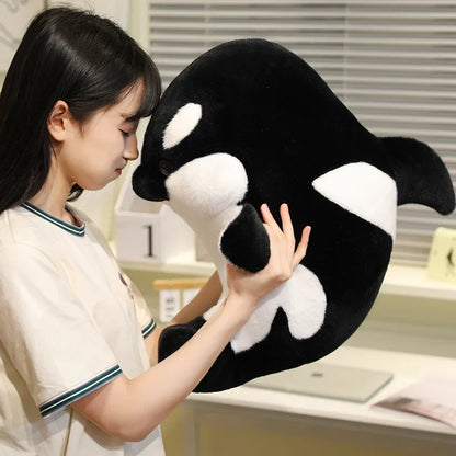 Black and white dolphin plush hugged by a person, open mouth fabric detail visible.