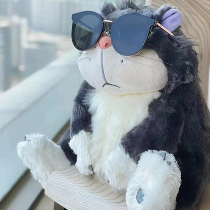 Plush cat doll wearing dark round sunglasses, dark gray fur with green eyes and purple ears