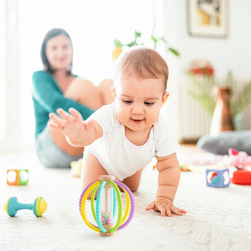 Baby rattle teether toy with rainbow silicone rings on wooden base on soft blanket