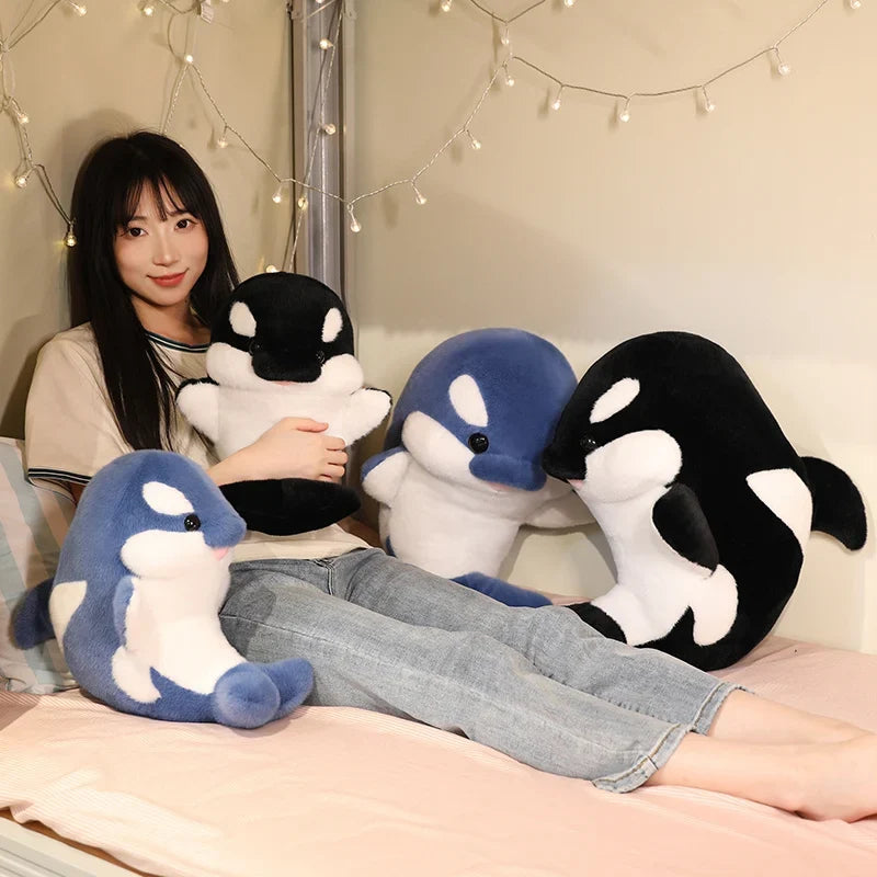 Blue and black dolphin plushies with white patches, three plush figures on a bed