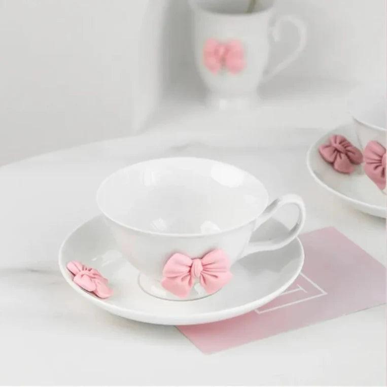 White tea cup with pink bow ornament on saucer, heart-shaped handles