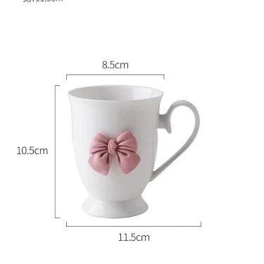 White coffee mug with pink bow on front and curved handle