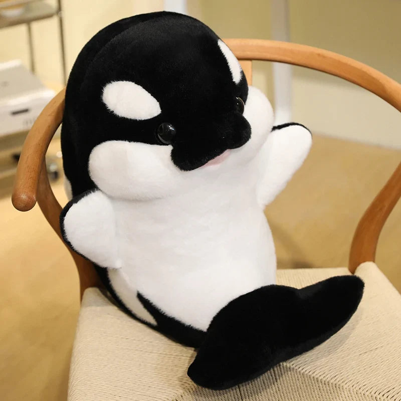 Black and white dolphin plush sitting on a chair seat with white belly patches.