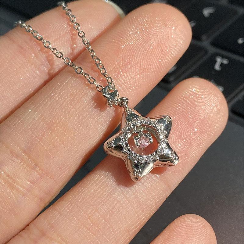 Silver star pendant necklace with pink center gem, shown held between fingers