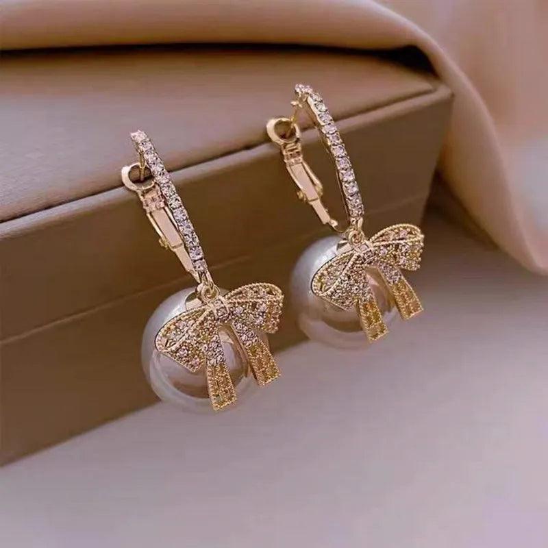 Gold-tone ornament hoop earrings with white baubles and gold ribbon bows