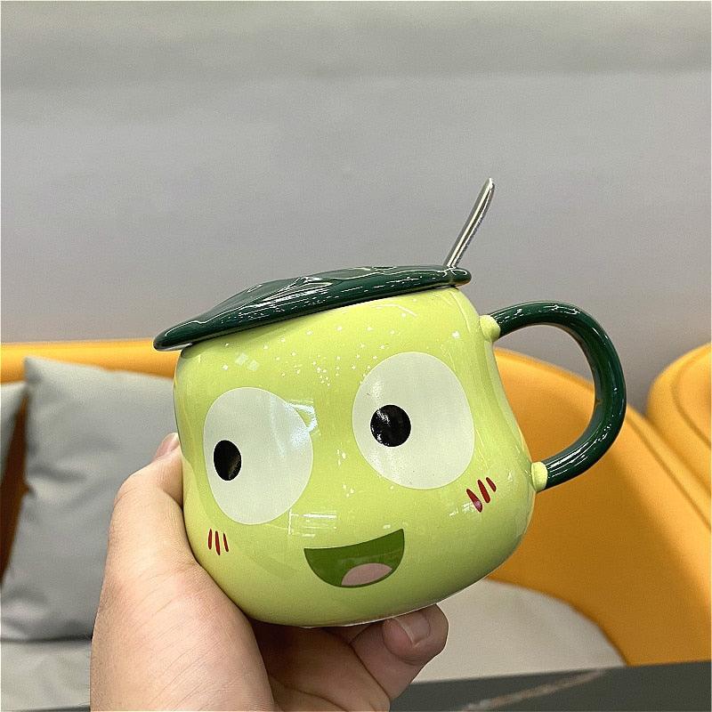 Lime green frog-shaped mug with lid and spoon, hand-held close-up with wide eyes and smile