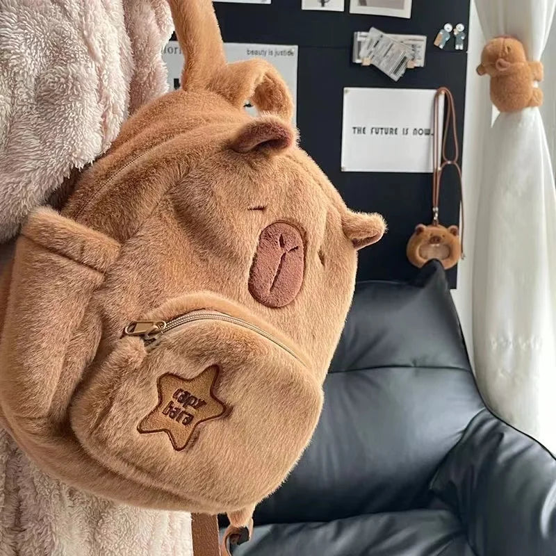 Tan capybara plush backpack with front zip pocket and star-shaped embroidered patch